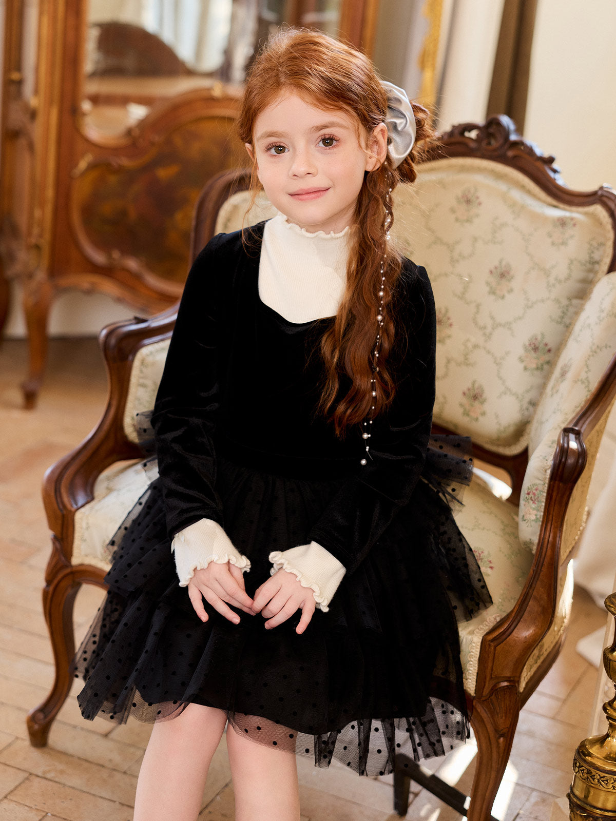 Seated styling view of the black velvet dress over a cream high-neck layer