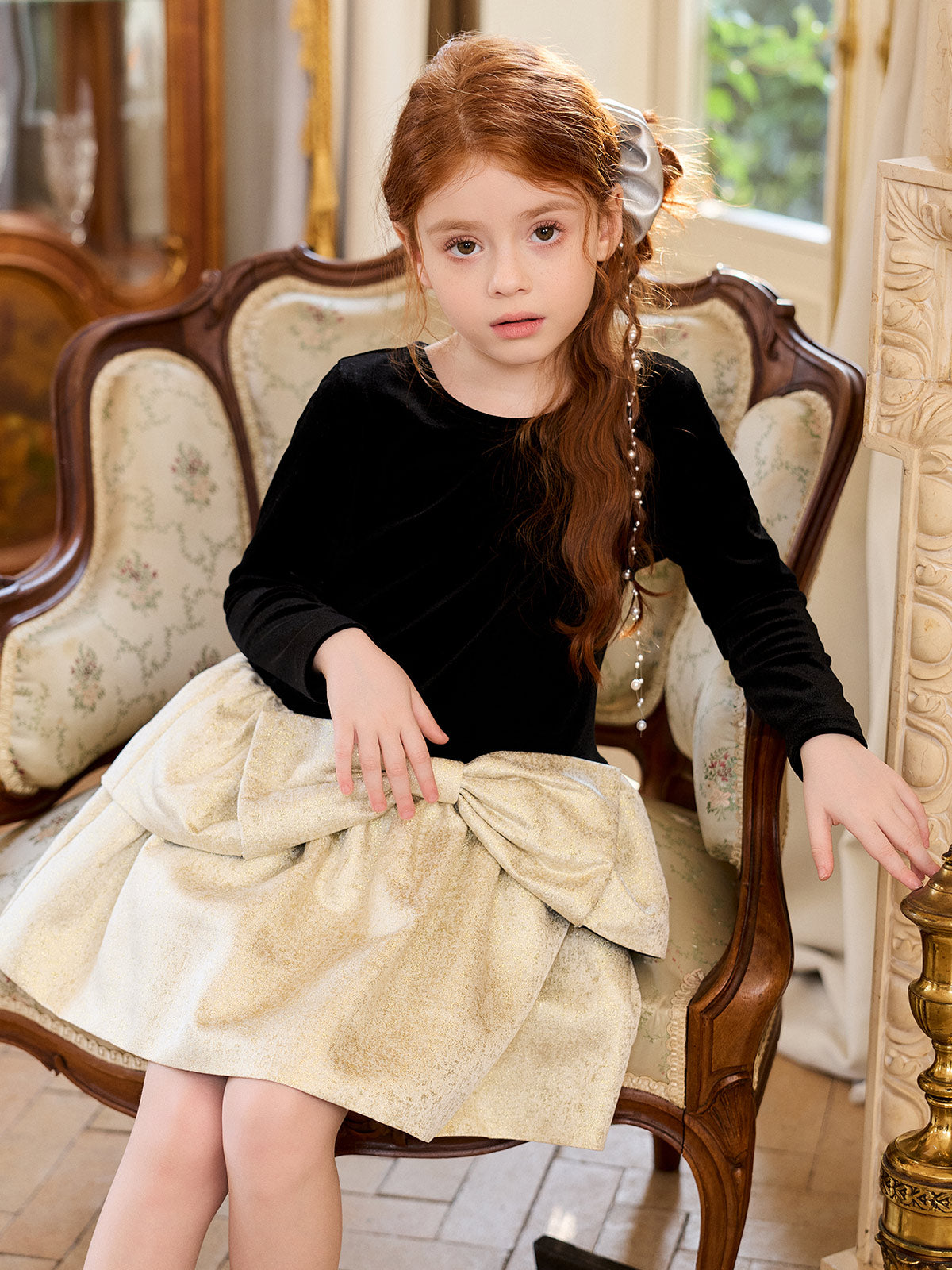Seated model showing the oversized champagne-gold waist bow